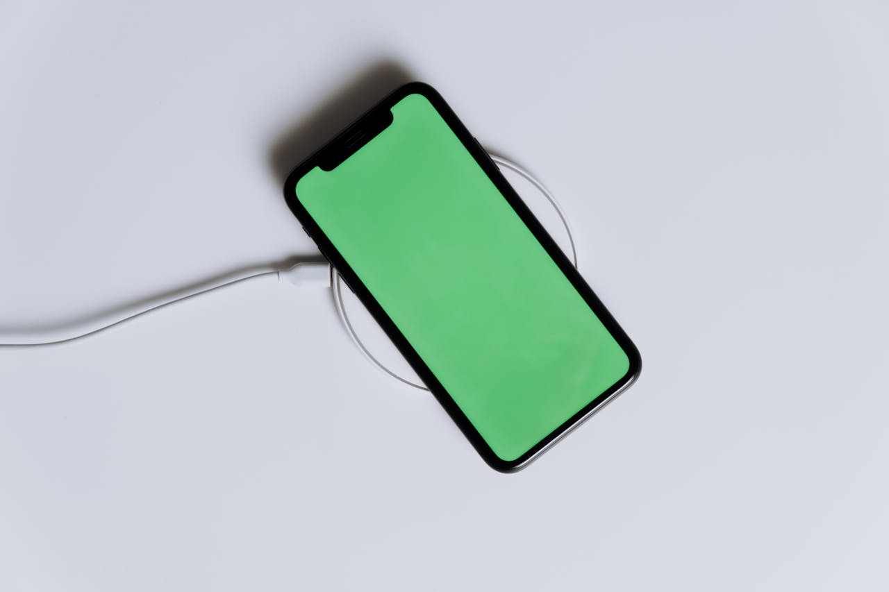 A minimalist smartphone with a green screen on a wireless charger, ideal for tech mockups.